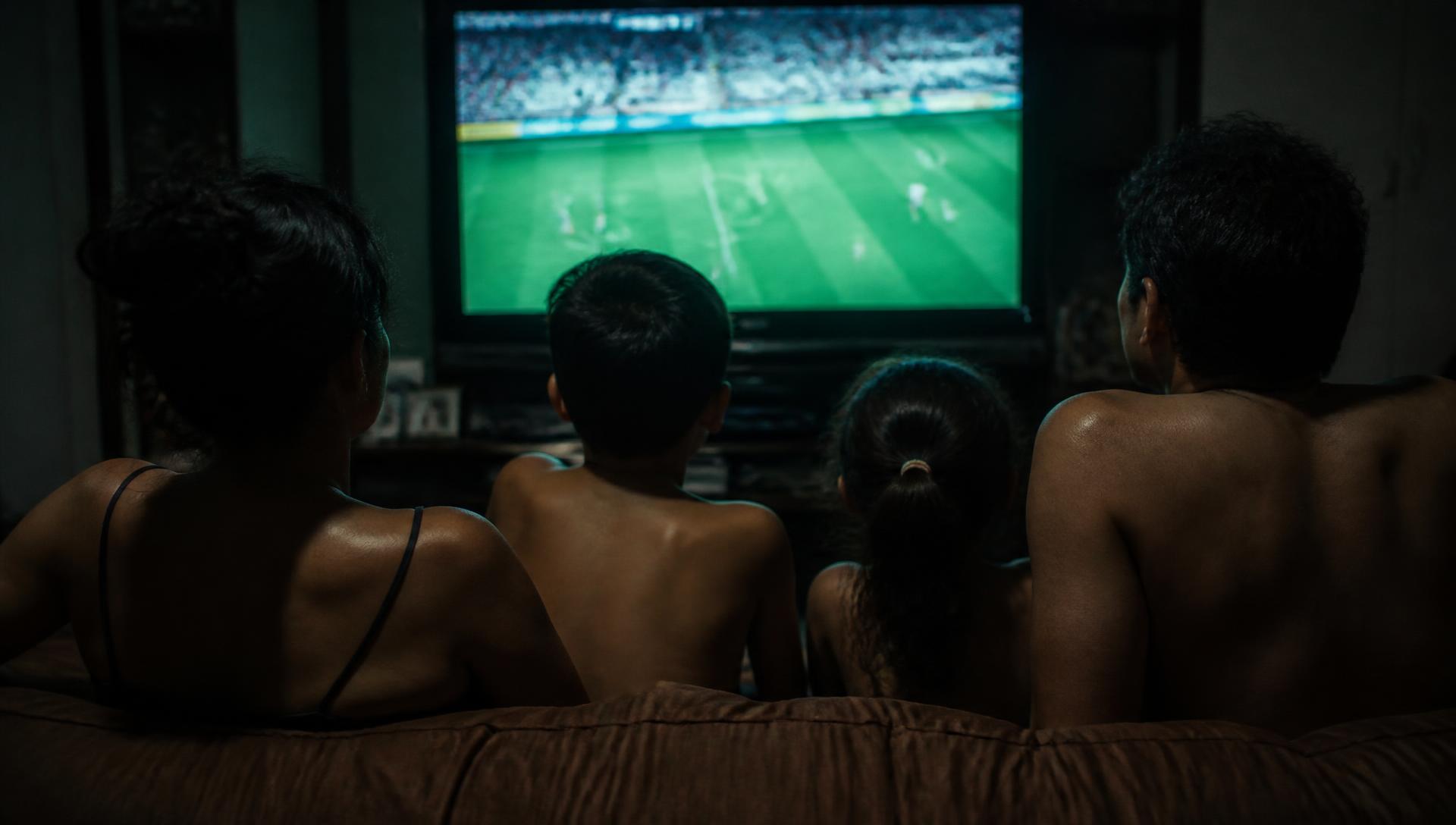Família assistindo televisão em uma sala escura com pipoca